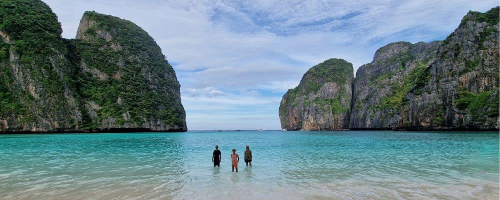 Kids stood in clear water in a bay part surrounded by rocks on a family gap year.