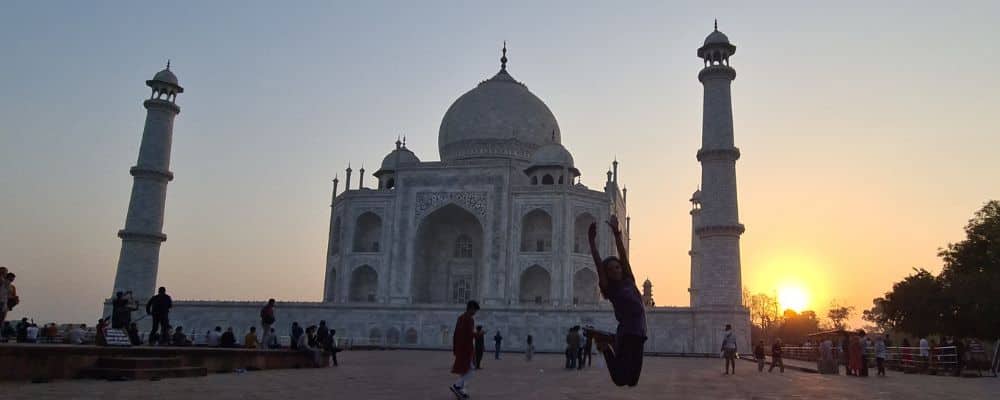 A kid jumping as the sun rises at an iconic elegant white mausoleum. This world wonder is visited by many.