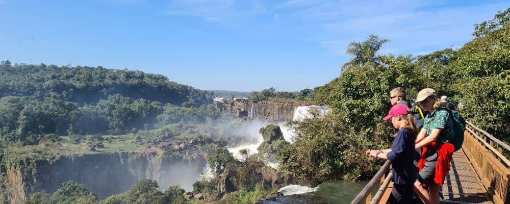 Kids looking out from a bridge to waterfall and green rainforest in the sun. A perfect gap year destination.