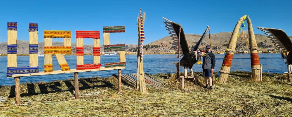 A kid stood with a large bird sculpture and the word Uros on a floating island on lake Titicaca, Peru with kids