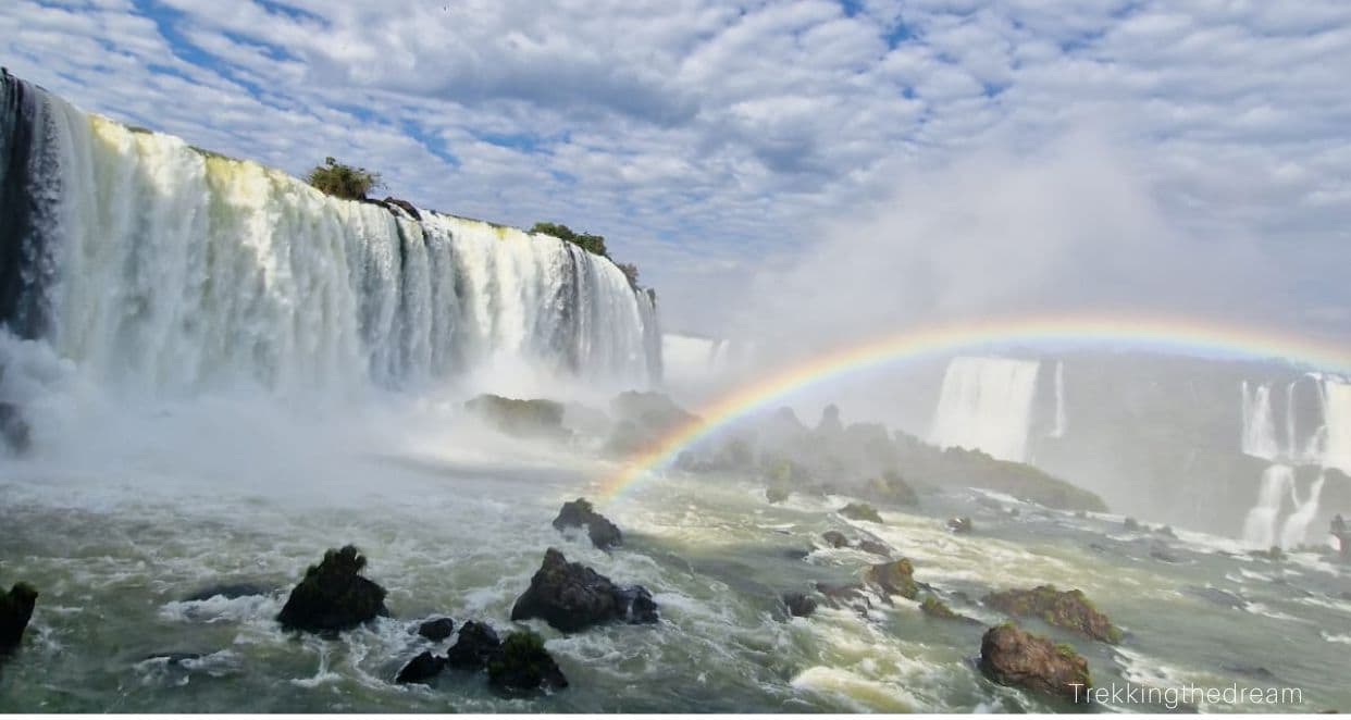 Cascading waterfalls with blue skies and a rainbow. Iguazu Falls is a must see when in Brazil with kids.