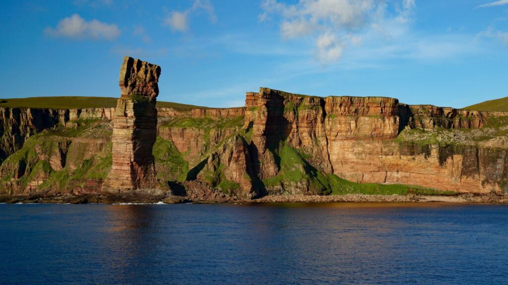 A tall stack of rock in the sea, overlooked by a cliff top hike.