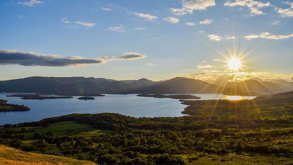 sun in the distance over Scottish mountains and loch