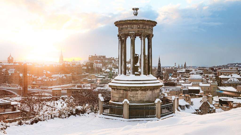 Snow on a monument with a city in the distance is a common sight it destinations across Northern Europe in winter.