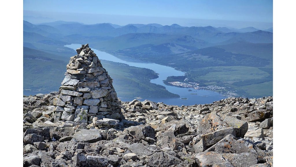 Mountain view over looking a Scottish loch. A cairn marks the path for hikers