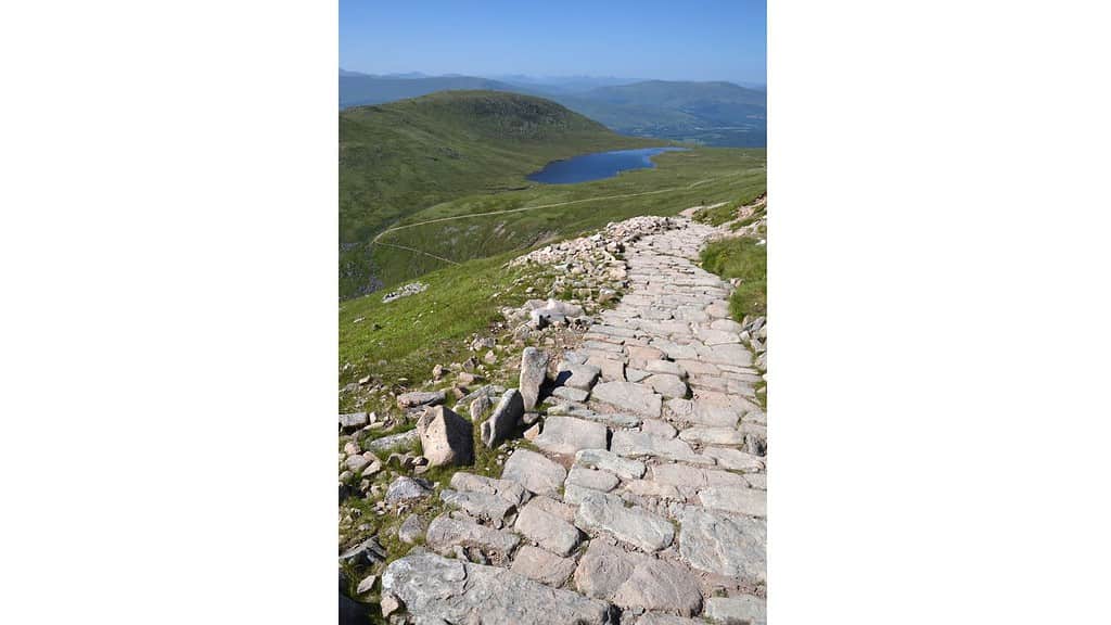 stone path descending a mountain with green hills and a loch.