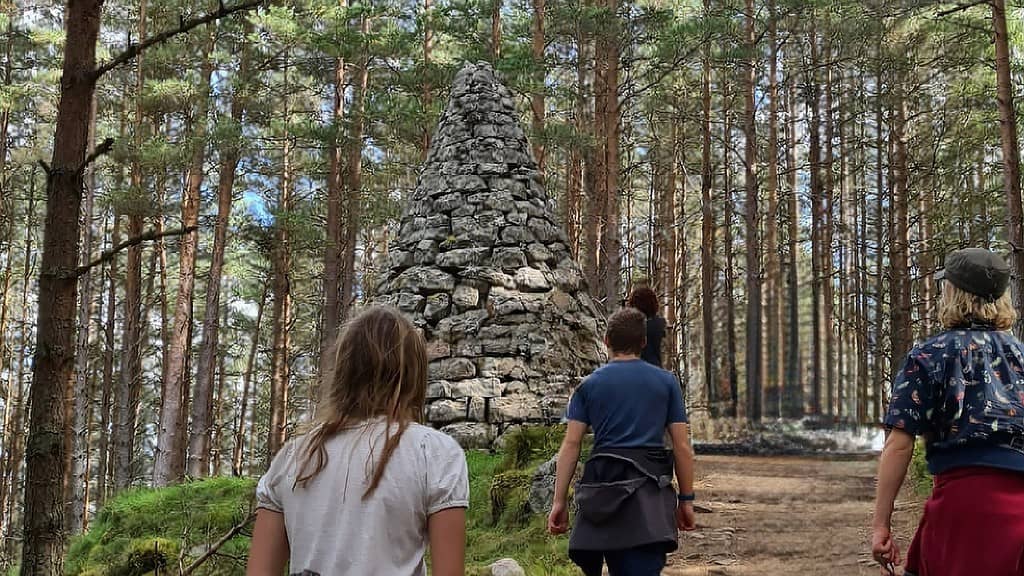 A family walking towards a stone kern in a woods.