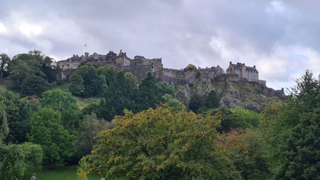 A large stone castle on top of a hill surrounded by park and green trees. Edinburgh Castle is one of the best castles to visit in Scotland.