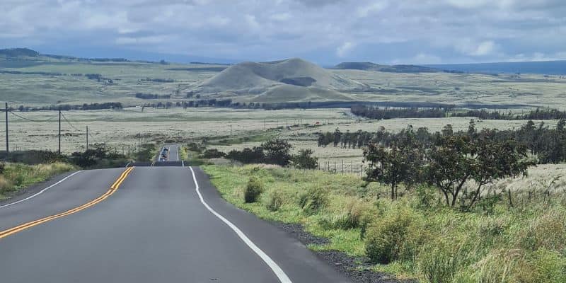 Straight road heading heading off surrounded by open green fields and hills on a road trip in Hawaii.