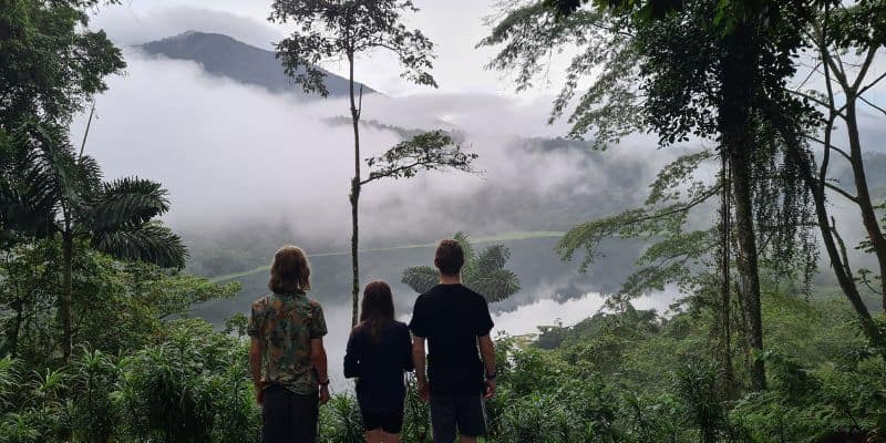 3 children stood in green forest looking out into a water filled volcanic crater with cloud. A perfect adventure by road