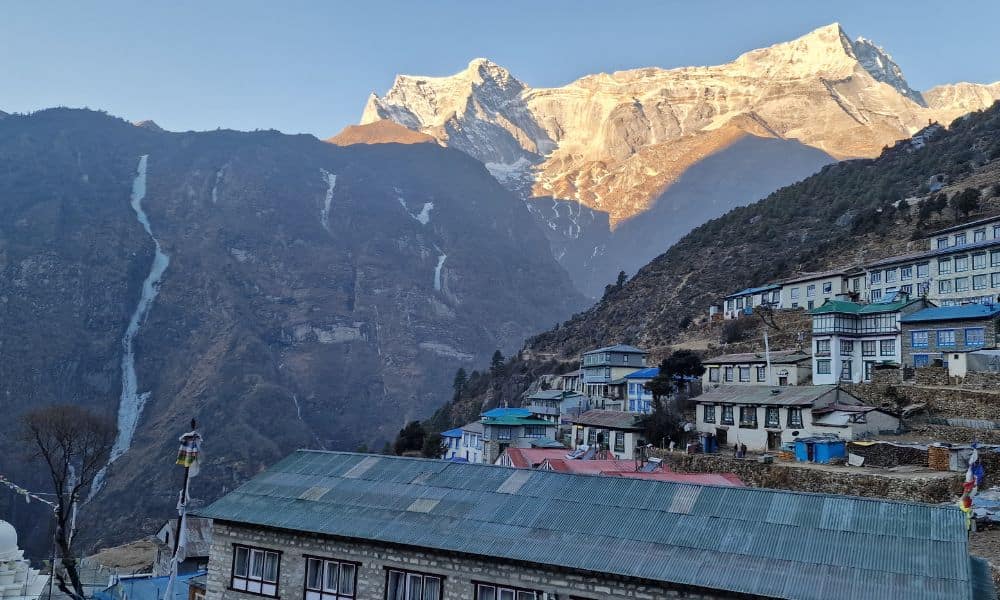 Mountainside village with mountains in the distance that sun is shining on. 