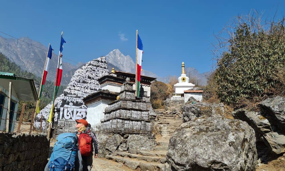 Kids trekking in Nepal near decorated stones and flags.