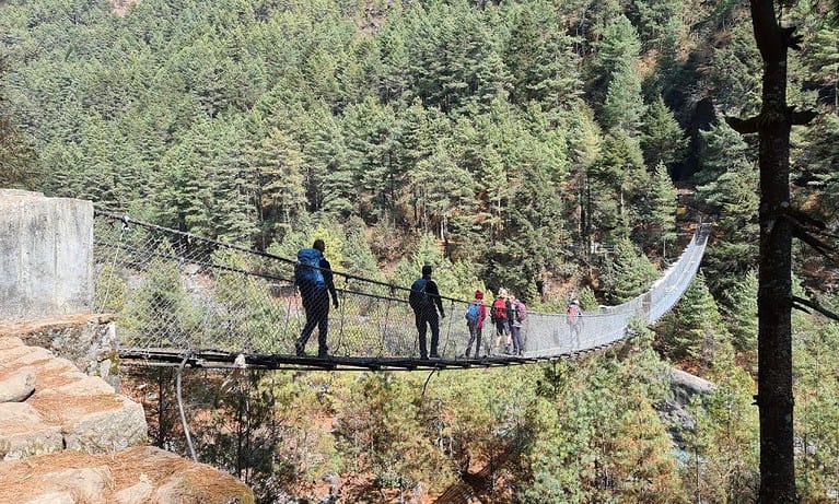 A family hiking a suspension bridge over a river surrounded by forest in Nepal on the way to Everest Base Camp.