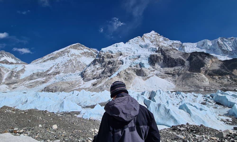 A person from the back stood in front of a glacier and mountains with clear blue sky at Everest base camp 