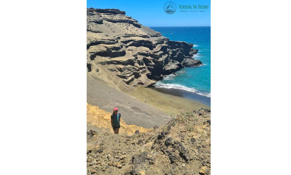 A girl stood on Green Sand Beach surrounded by rock and ocean.