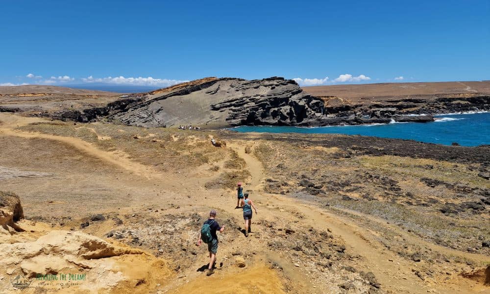 Family walking a dirt track with Papakolea Beach in front of them