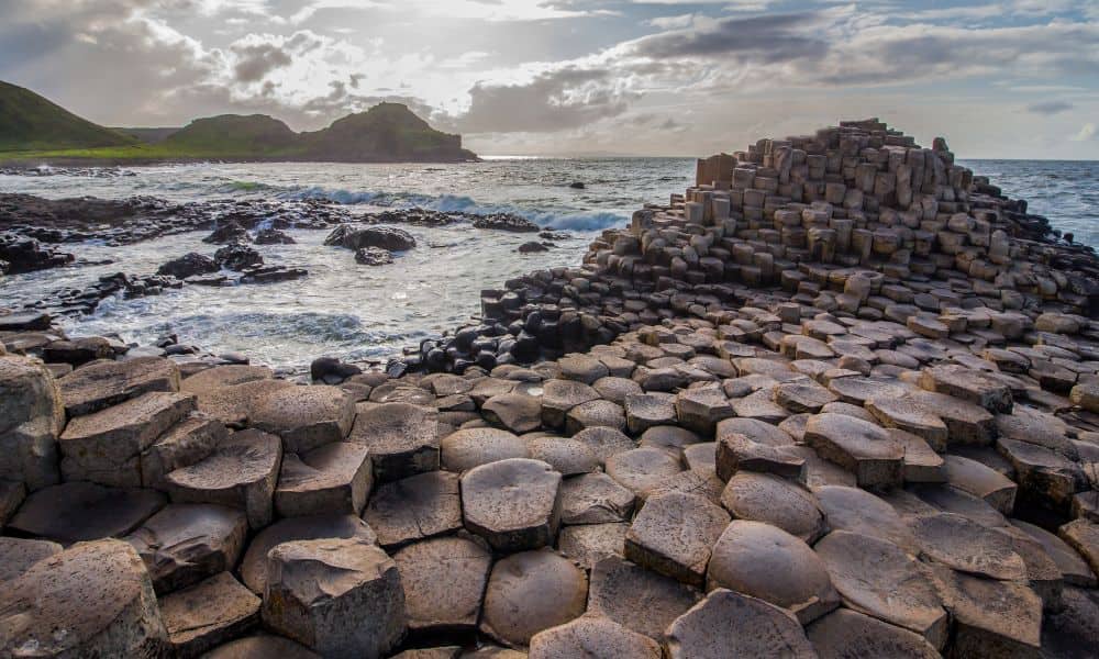 Hexagonal basalt stepped columns and ocean with a cloudy sky. The Giant's Causeway is an ideal place to visit in the UK with kids.