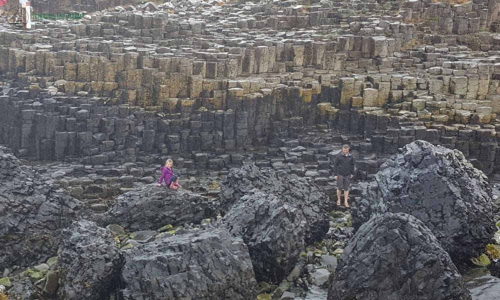 Kid with man stood on rock formations that are worth seeing at the Giant's Causeway