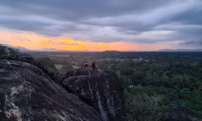 A family sat on a large rock overlooking jungle at sunset in Sri Lanka.