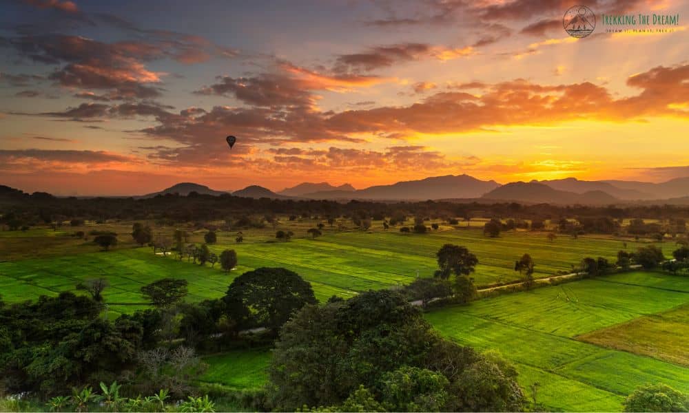 Hot air balloon floating over green fields as orange sun raise are rising over the hills.
Canva