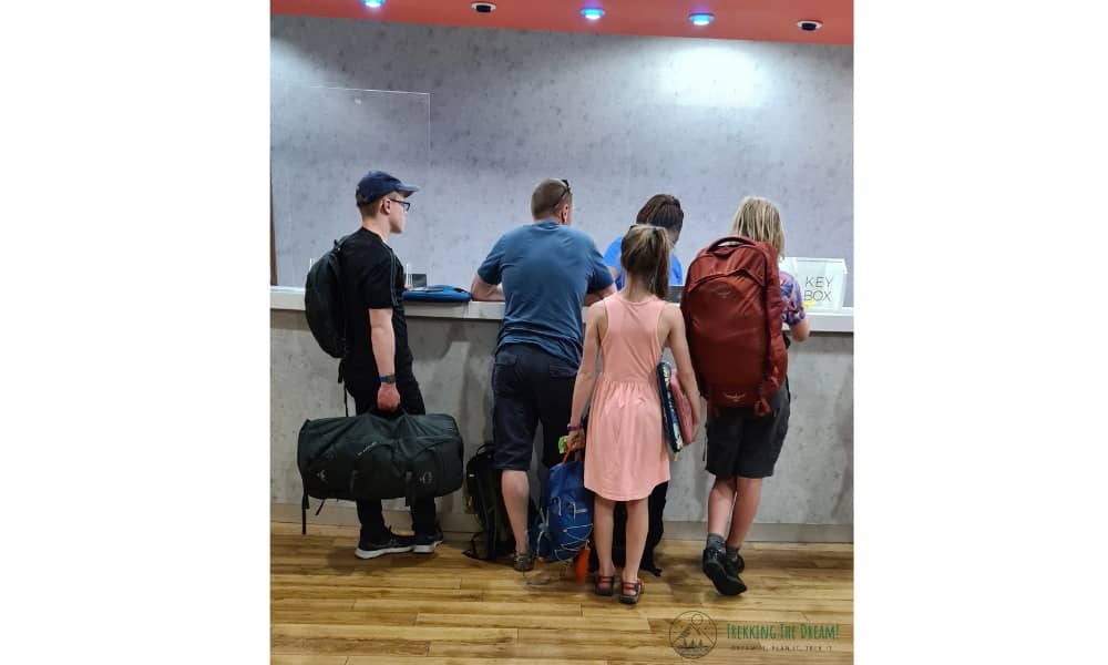 Family standing at a desking with hand luggage to make travel more affordable with kids.