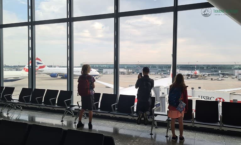 Children watching aeroplanes from an airport window before flying on their family adventure.