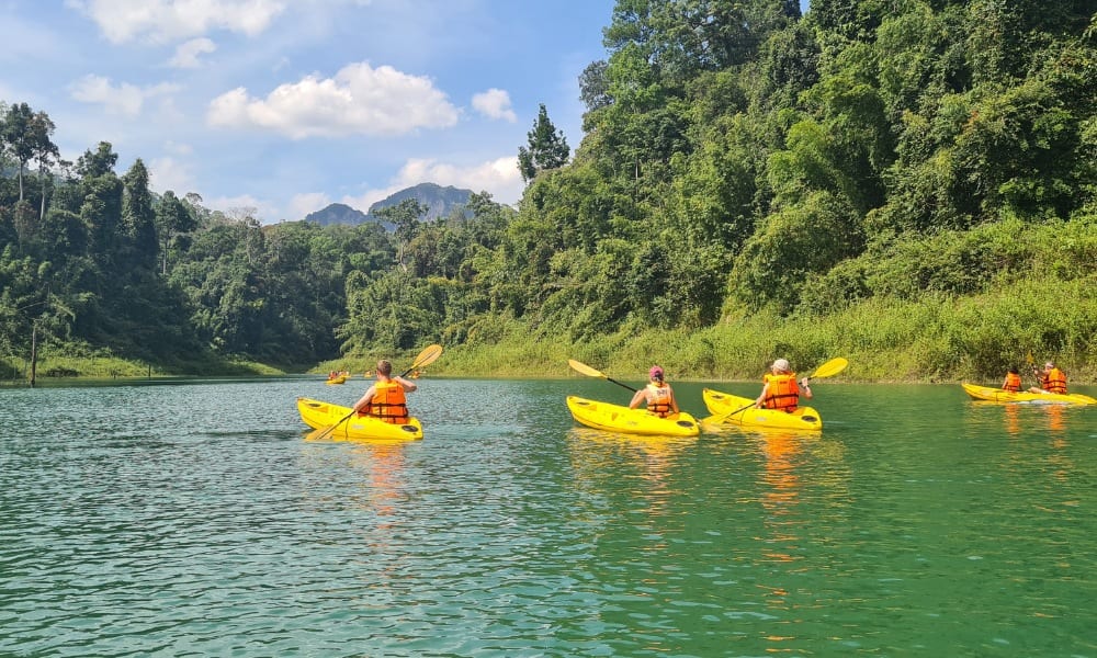 A family kayaking on a green lake in front of green jungle.