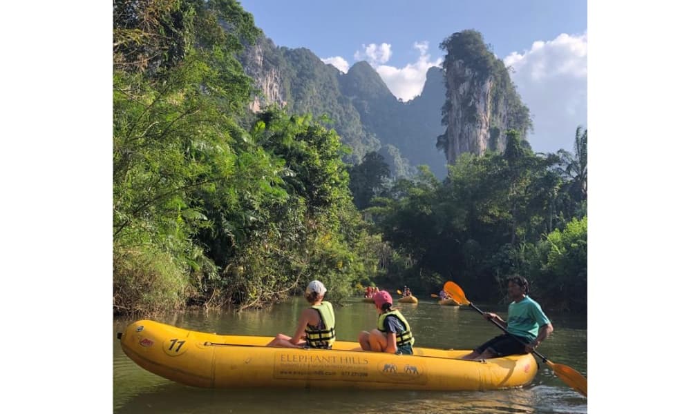 People in a paddled boat on a river surrounded by jungle and hills