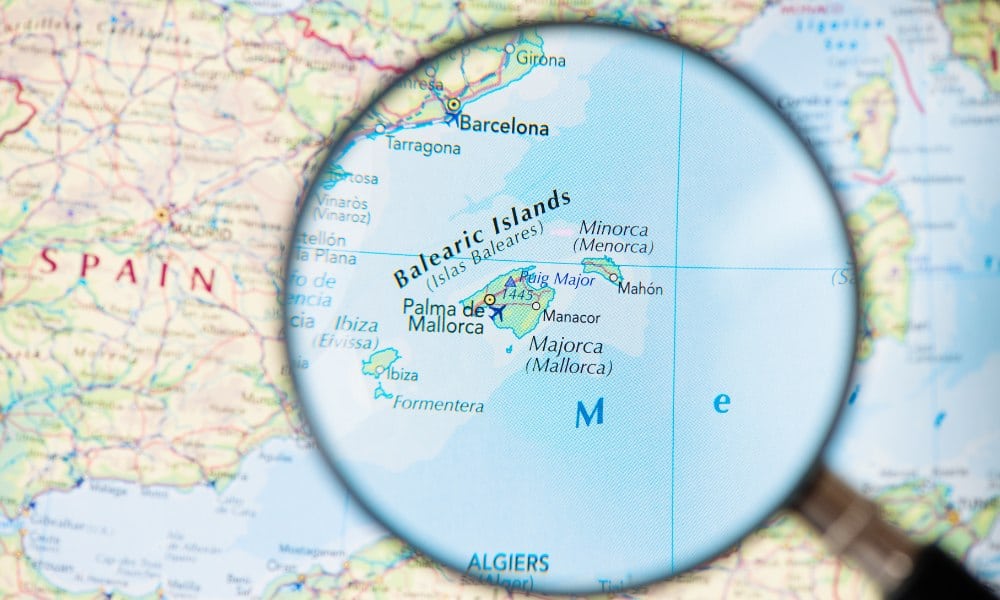 A blue, yellow and green map of Europe and a magnifying glass highlighting the Balearic Islands including Ibiza.