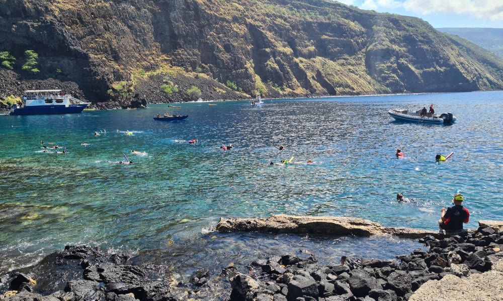 Open bay of ocean part surrounded by rock and hills on a sunny day. People are snorkeling in Kealaekua Bay, Hawaii