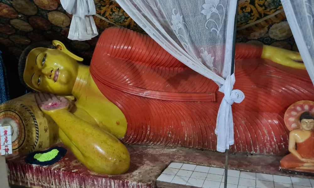 yellow reclined Buddah wearing red with white netting tied. An important temple on Pidurangala.