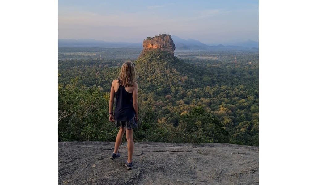 Kid stood on a rock over looking jungle and a protruding rock. 