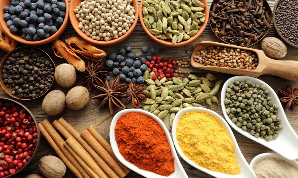 A selection of yellow, orange, red, green, brown and black spices laying on a table ready to be used in a traditional dish.