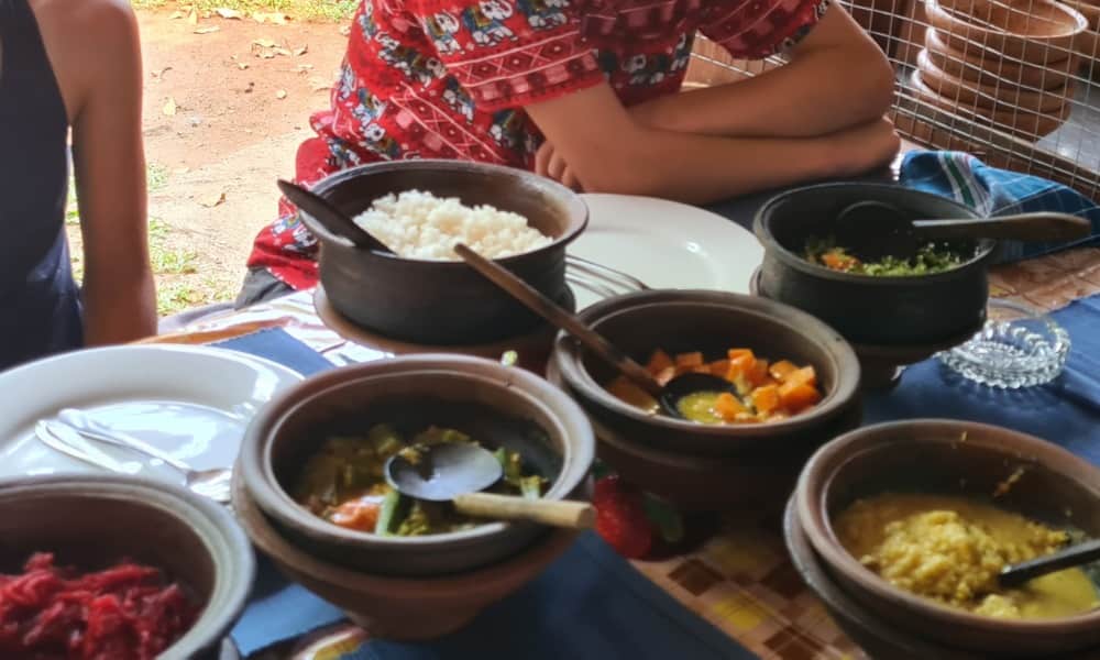 Kids sat at a table with six bowls of different Sri Lankan Food including rice, vegetable curry and dahl.