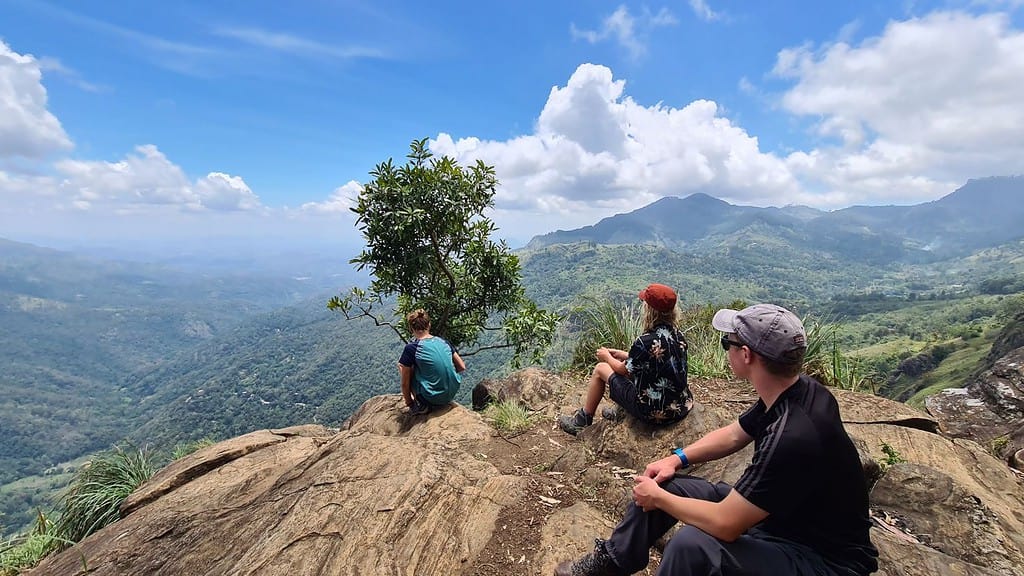 kids sat at the top of a rock over looking stunning views of hills with blue sky and white clouds. Ella Rock viewpoint.