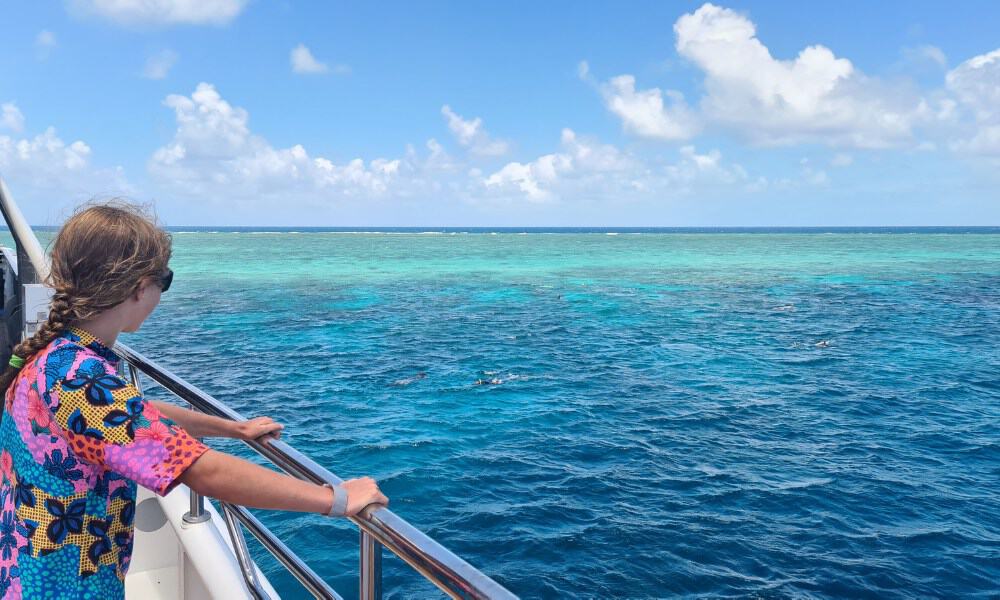 A girl stood on a boat looing out to a blue sea with blue sky and white fluffy clouds. Great views at the Great Barrier Reef Australia.