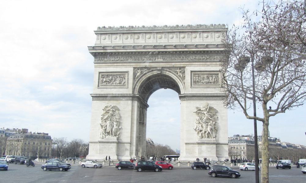 Large white arch surrounded by cars driving round the road. An iconic building in Paris.