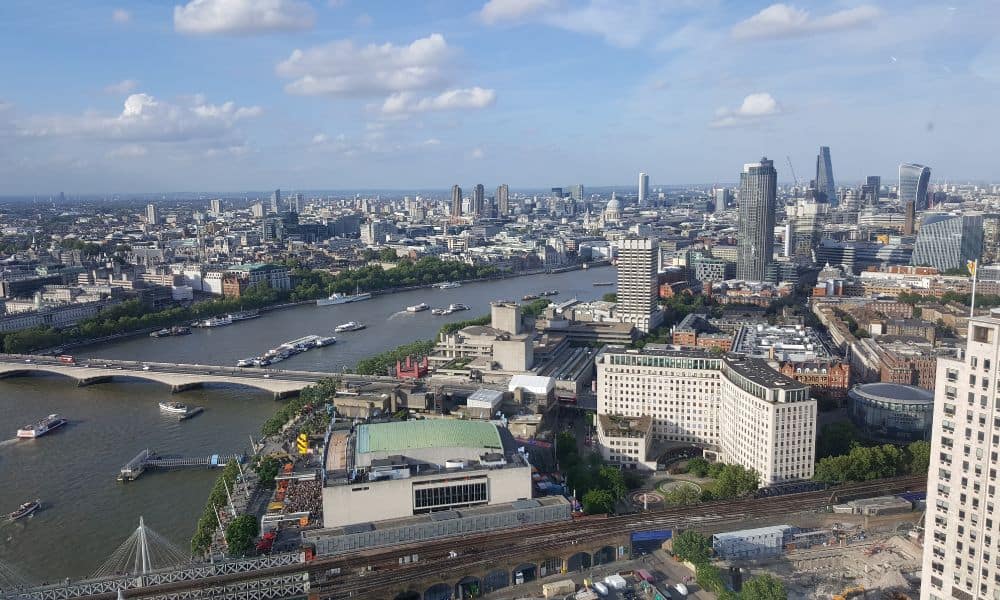 Wide river with boats flowing through a high rise city. The River Thames is a landmark in London.