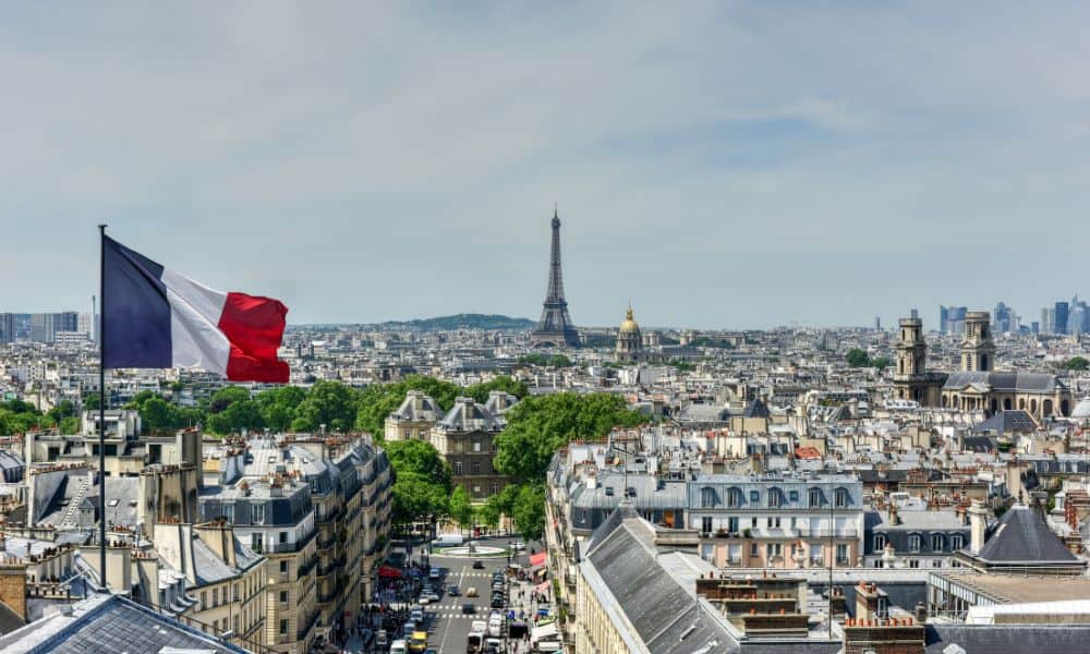 City skyline with a blue, white and red french striped flag flying and a tall structure towering above the city of Paris 