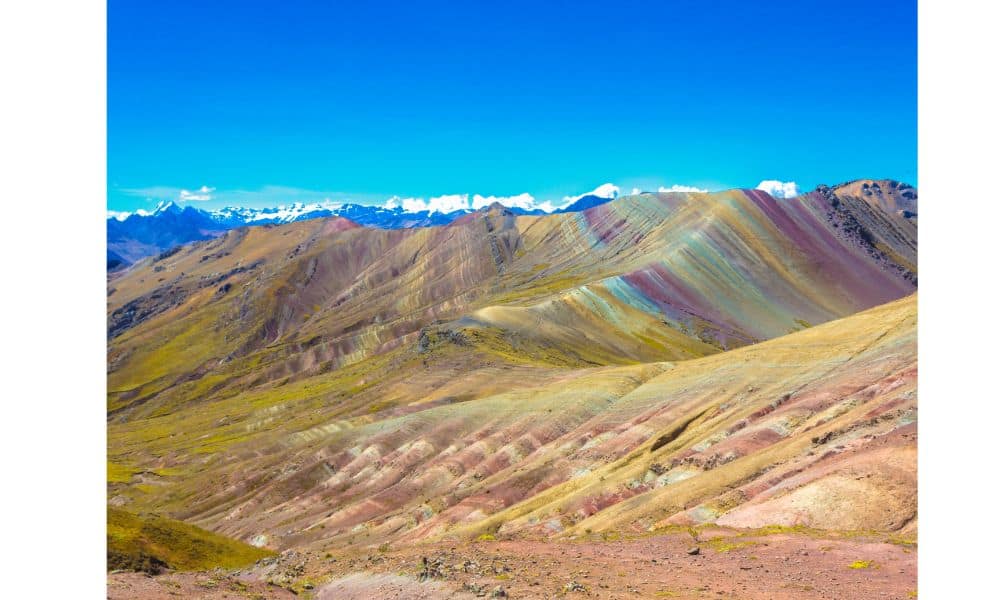 Sandy mountains with striped colours of purple, green, yellow and pink with blue sky. Visiting here is a great thing to do in Peru.