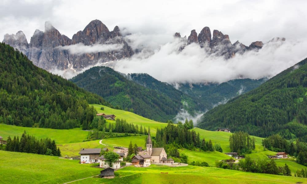 A small village surrounded by green rolling hills and striking grey mountains covered in mist. The diversity of Italy's landscapes are a reason to visit.