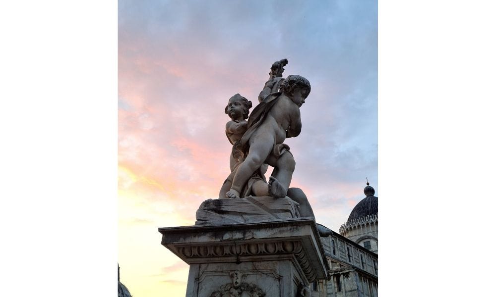 A statue of two cherubs on a platform with a cloudy sky at sunset in Italy. Art is a reason to visit Italy.