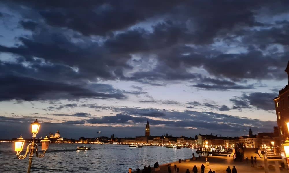 Landscape of ocean surrounded by illuminated walkways and buildings. A view from Venice Italy at dusk.