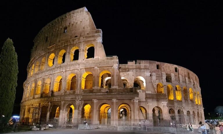 Large round stone building with glassless windows with dark night sky. The iconic Roman Colosseum in italy is worth seeing.