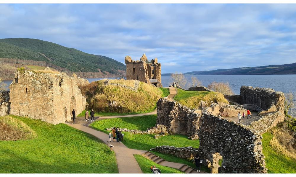 Ruined castle in Scotland surrounded by green grass and a large loch. 