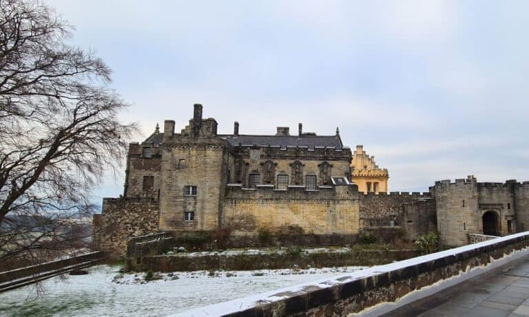 A grand castle sat on a hill in Scotland with some snow.