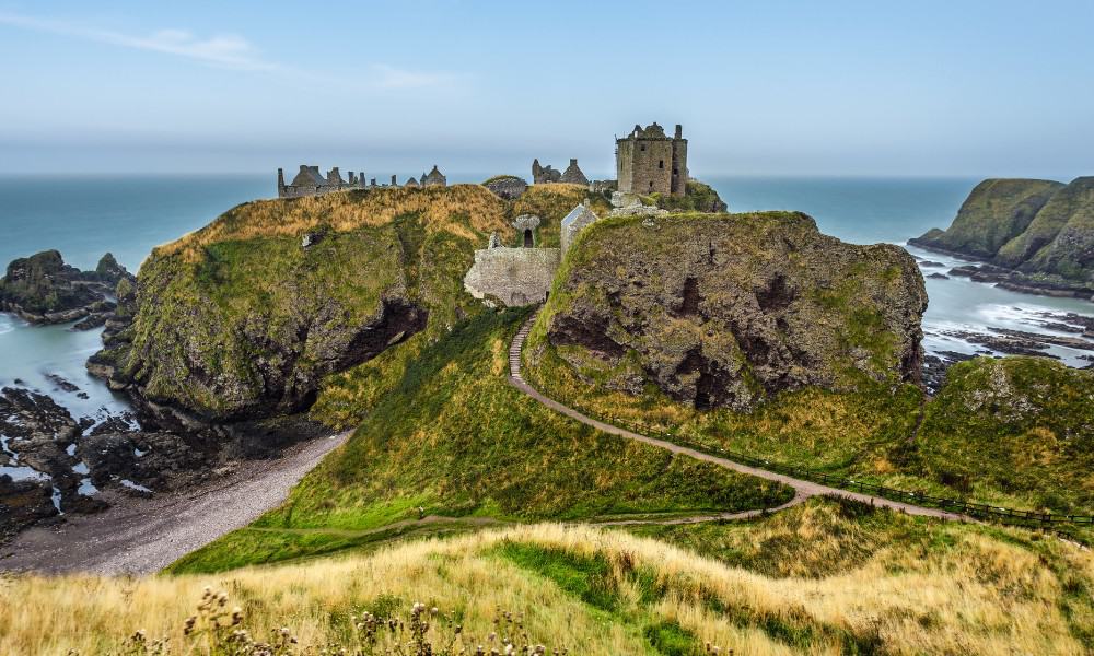 A stunning castle sat on a hill overlooking the sea surrounded by green grass. One of the best castles in Scotland