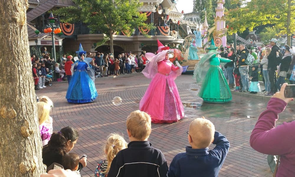 Trekking The Dream Family watching a parade on the street at Disneyland with a pink, green and blue fairies and a castle float.