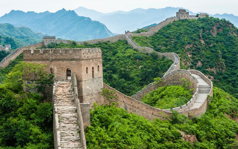 Long winding stone wall through lush green fields in China. Many people visit this wonder of the world. 