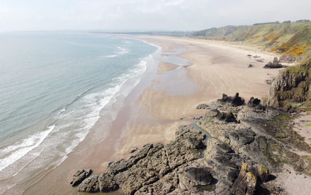 A long sandy beach with sea and a rocky cliff iconic of beaches in Scotland